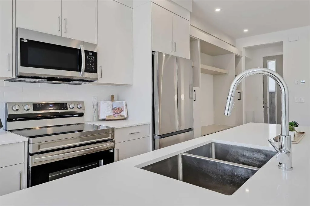 Kitchen sink, gas range, and built-in fridge with white cabinetry